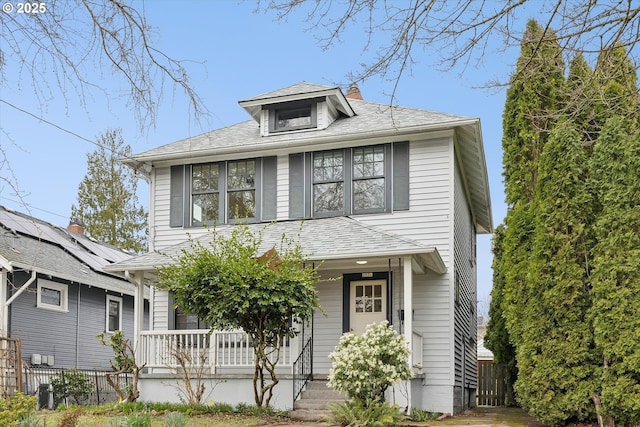 american foursquare style home featuring a porch, a shingled roof, a chimney, and fence