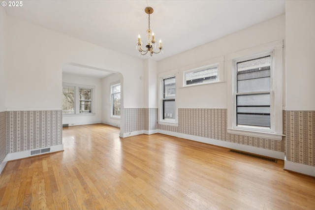 spare room with an inviting chandelier, light wood-style floors, visible vents, and wainscoting