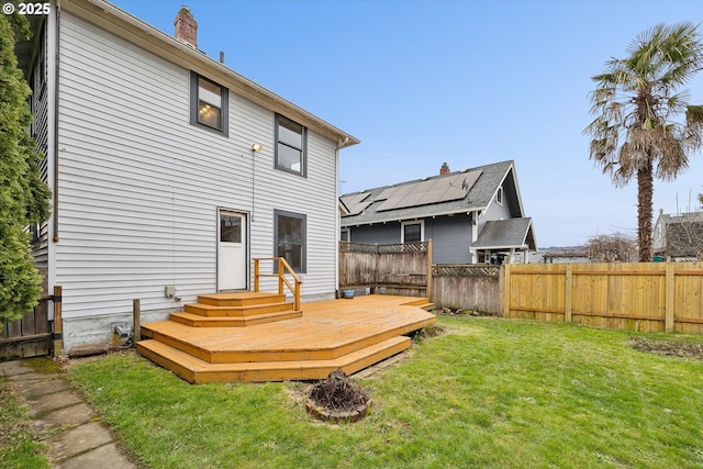 rear view of house with a yard, a deck, a chimney, and fence