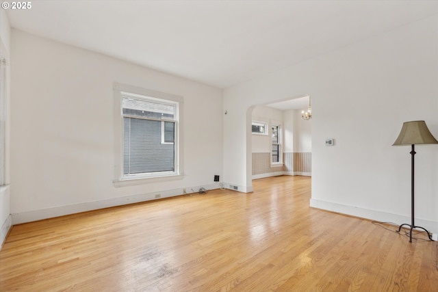 empty room featuring light wood-type flooring, visible vents, a notable chandelier, arched walkways, and baseboards