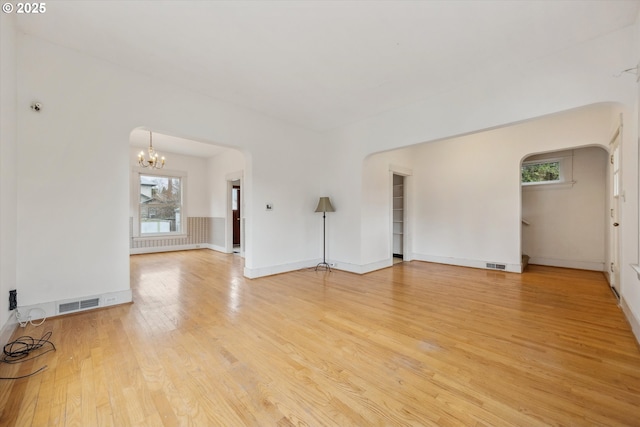 unfurnished living room featuring visible vents, baseboards, a notable chandelier, and light wood-style flooring