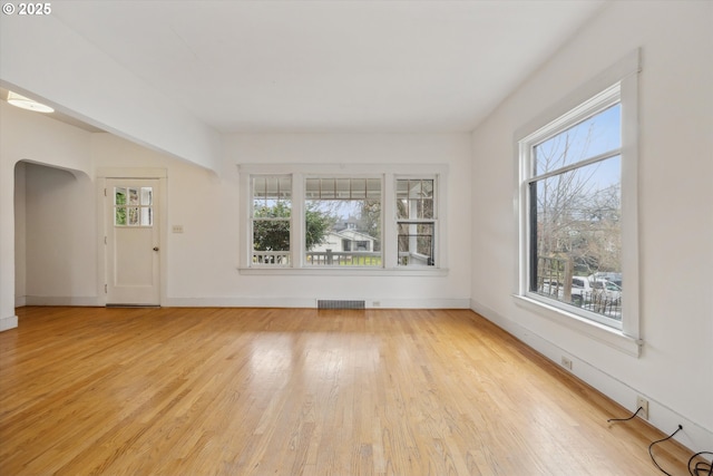 spare room with arched walkways, visible vents, baseboards, and light wood-style floors