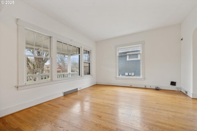 empty room with baseboards, wood finished floors, visible vents, and arched walkways