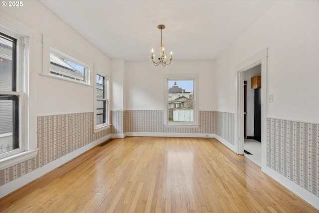 unfurnished room with visible vents, wallpapered walls, wainscoting, an inviting chandelier, and wood-type flooring