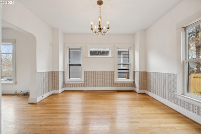 unfurnished dining area with wallpapered walls, a notable chandelier, light wood finished floors, and wainscoting