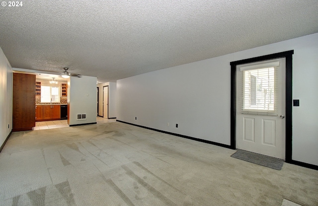 unfurnished living room featuring ceiling fan, light colored carpet, a textured ceiling, and a healthy amount of sunlight