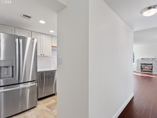 kitchen with appliances with stainless steel finishes, a premium fireplace, light hardwood / wood-style floors, and white cabinetry