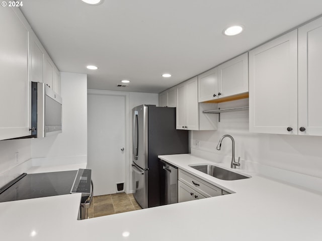 kitchen with stainless steel appliances, white cabinetry, light tile patterned floors, and sink