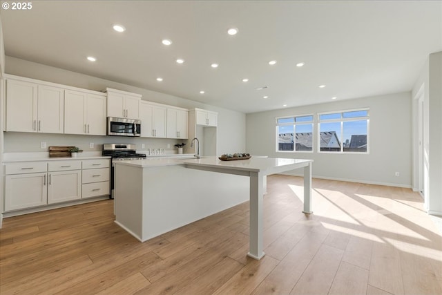 kitchen with light wood-type flooring, white cabinetry, a center island with sink, and appliances with stainless steel finishes