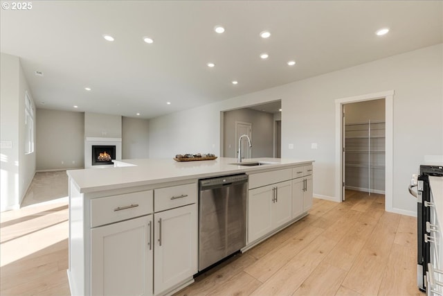 kitchen with appliances with stainless steel finishes, white cabinetry, sink, light hardwood / wood-style flooring, and a center island with sink