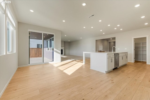 kitchen with stainless steel dishwasher, a kitchen island with sink, light wood-type flooring, and white cabinets