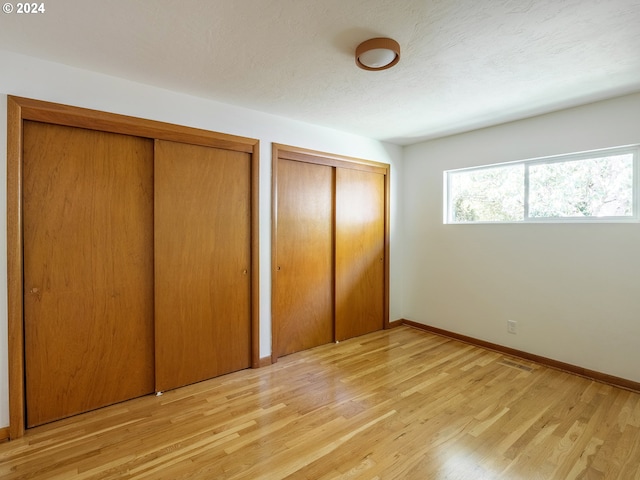 unfurnished bedroom featuring a textured ceiling, light hardwood / wood-style flooring, and multiple closets