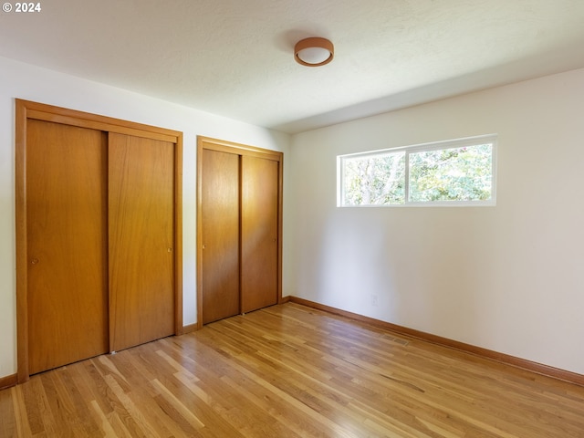 unfurnished bedroom with two closets and light hardwood / wood-style flooring