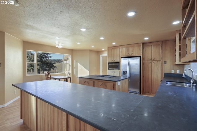 kitchen featuring sink, light hardwood / wood-style flooring, appliances with stainless steel finishes, a center island, and a textured ceiling