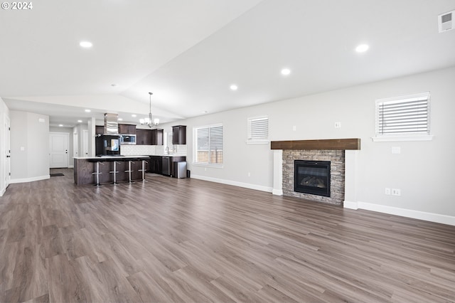 living room featuring lofted ceiling, a stone fireplace, dark wood-type flooring, sink, and a notable chandelier