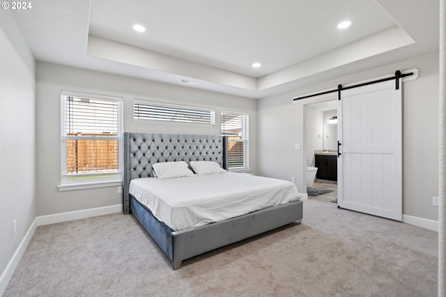 bedroom with a raised ceiling, connected bathroom, a barn door, and carpet