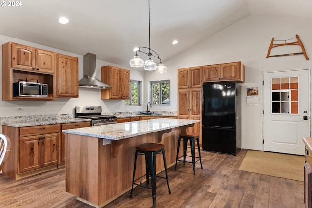 kitchen featuring appliances with stainless steel finishes, wall chimney exhaust hood, vaulted ceiling, and a center island