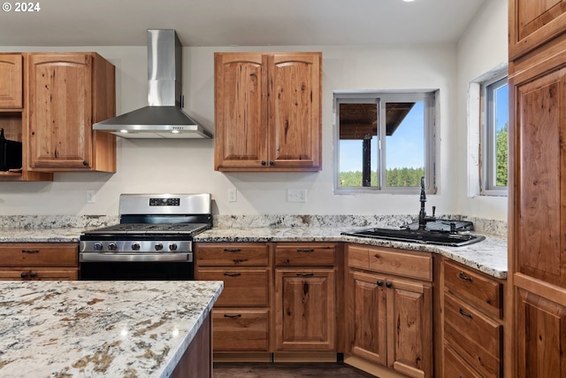 kitchen featuring light stone countertops, gas stove, wall chimney range hood, and sink