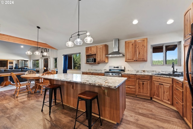 kitchen featuring lofted ceiling, sink, wall chimney range hood, appliances with stainless steel finishes, and a center island