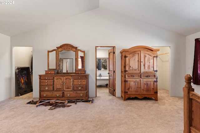 bedroom with a spacious closet, vaulted ceiling, light colored carpet, and ensuite bath