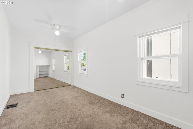 unfurnished bedroom with ceiling fan, a closet, crown molding, and carpet flooring