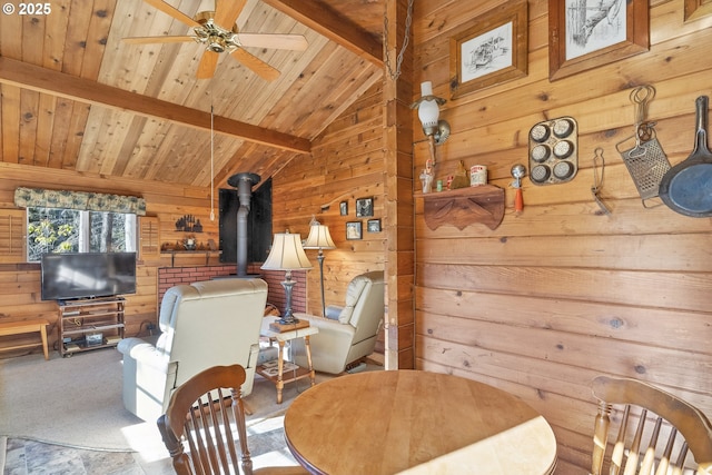 carpeted dining room featuring vaulted ceiling with beams, a ceiling fan, a wood stove, wood walls, and wooden ceiling