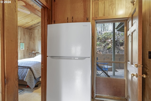 kitchen with lofted ceiling, freestanding refrigerator, wood ceiling, and wooden walls