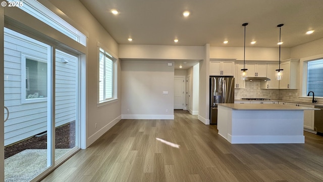 13910 SW 166th Ave, Tigard, OR 97223 - kitchen with stainless steel appliances, a kitchen island, under cabinet range hood, backsplash, and wood finished floors