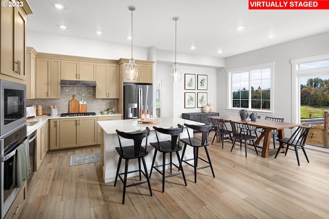 kitchen with a center island, light hardwood / wood-style floors, decorative backsplash, hanging light fixtures, and stainless steel appliances