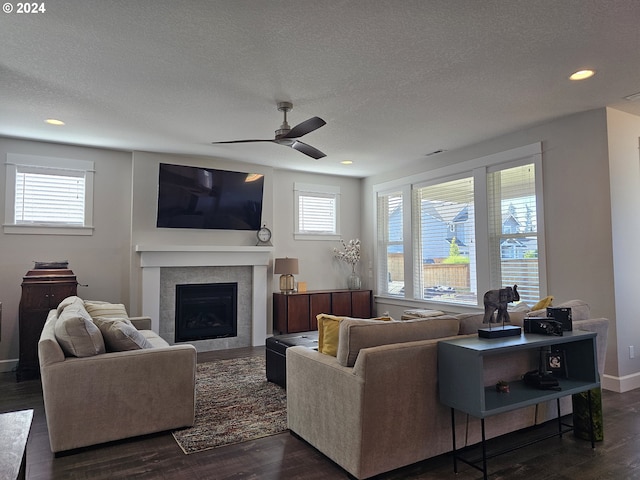 living room featuring a textured ceiling, ceiling fan, dark wood-type flooring, and a tiled fireplace