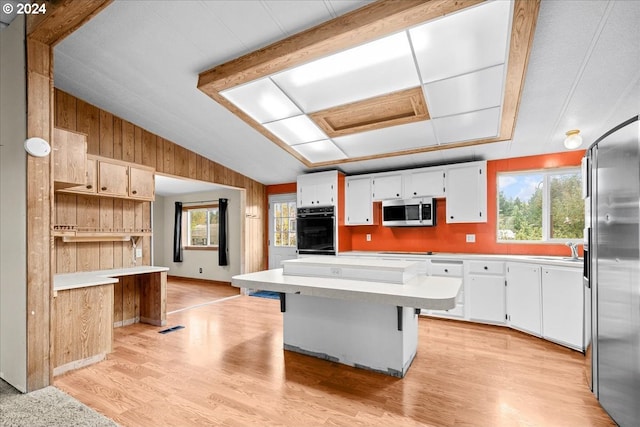 kitchen featuring stainless steel appliances, white cabinets, a center island, a kitchen bar, and light wood-type flooring