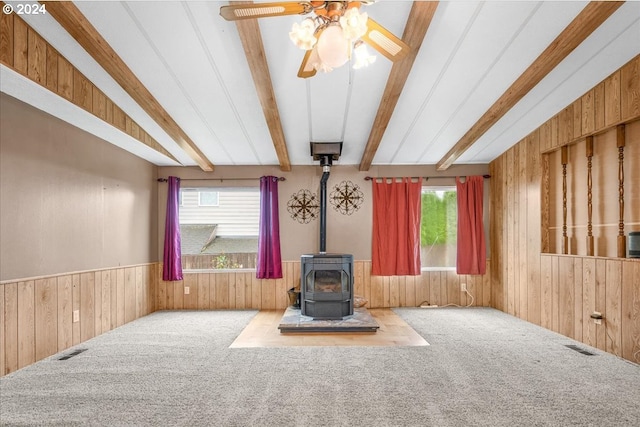 unfurnished living room with carpet floors, ceiling fan, a wood stove, and wooden walls