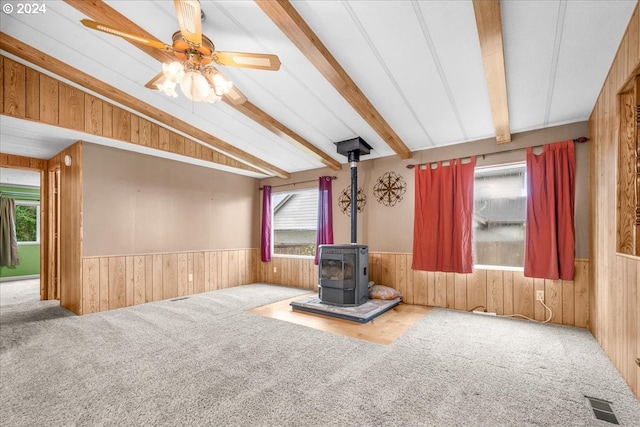 unfurnished living room featuring vaulted ceiling with beams, carpet floors, ceiling fan, and a wood stove