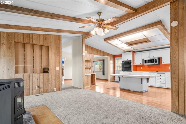 kitchen featuring white cabinetry, a wood stove, light carpet, ceiling fan, and a breakfast bar