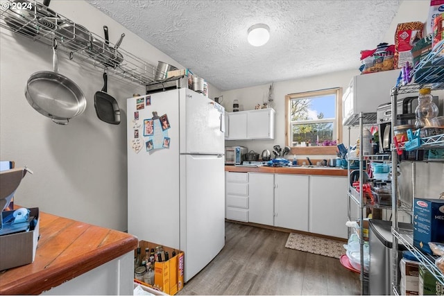 kitchen featuring hardwood / wood-style floors, white refrigerator, a textured ceiling, and white cabinetry