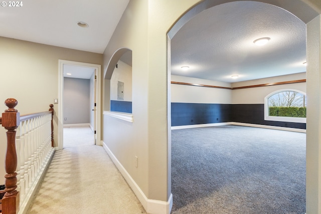 hallway with light carpet and a textured ceiling