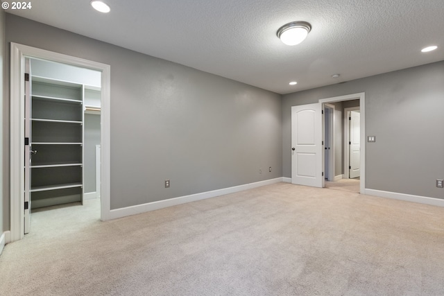 unfurnished bedroom with a spacious closet, a closet, light carpet, and a textured ceiling