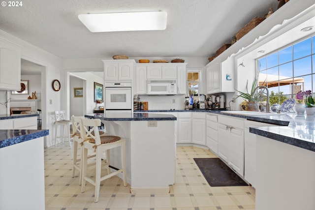 kitchen with a textured ceiling, white appliances, sink, a center island, and white cabinetry