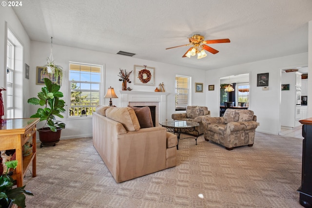 carpeted living room with a tile fireplace, ceiling fan, and a textured ceiling