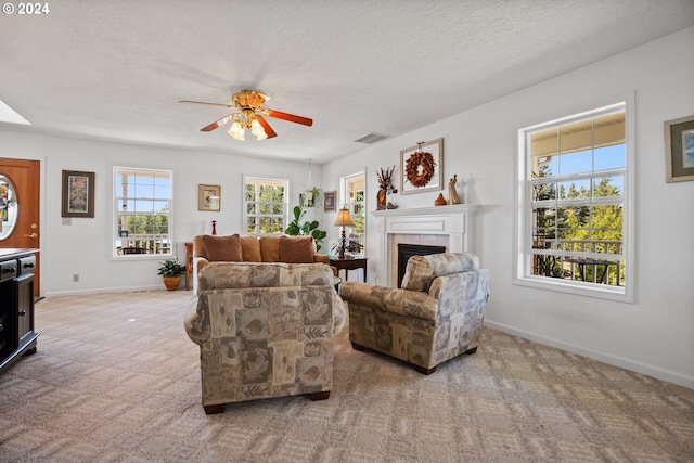 living room featuring ceiling fan, a textured ceiling, light carpet, and a tiled fireplace