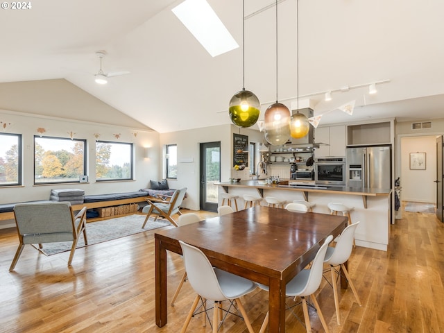 dining room featuring lofted ceiling with skylight, light wood-type flooring, and ceiling fan