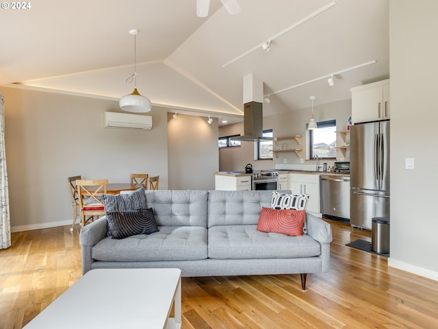 living room with light wood-type flooring, a wall unit AC, lofted ceiling, and rail lighting