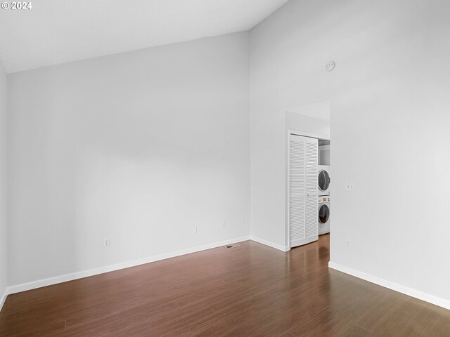 empty room featuring stacked washer / drying machine and dark hardwood / wood-style flooring