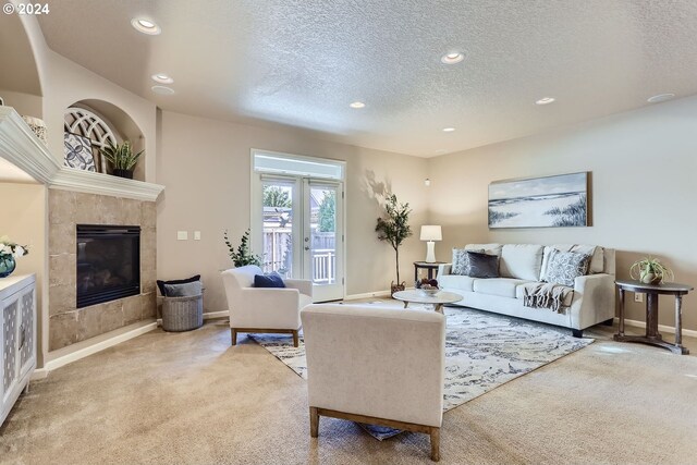 living room with a tiled fireplace, light colored carpet, and a textured ceiling