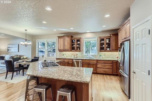 kitchen featuring a kitchen breakfast bar, light stone counters, a chandelier, light hardwood / wood-style floors, and appliances with stainless steel finishes