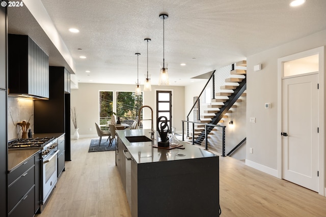 kitchen with decorative light fixtures, a center island with sink, sink, light wood-type flooring, and range with gas cooktop