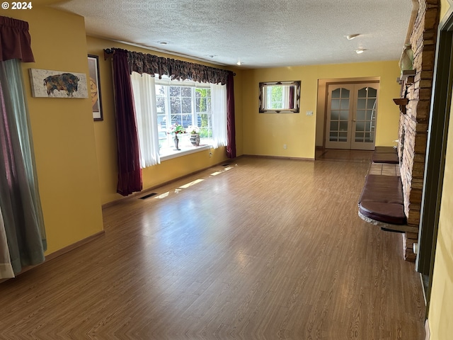 unfurnished living room featuring a fireplace, a textured ceiling, french doors, and wood-type flooring