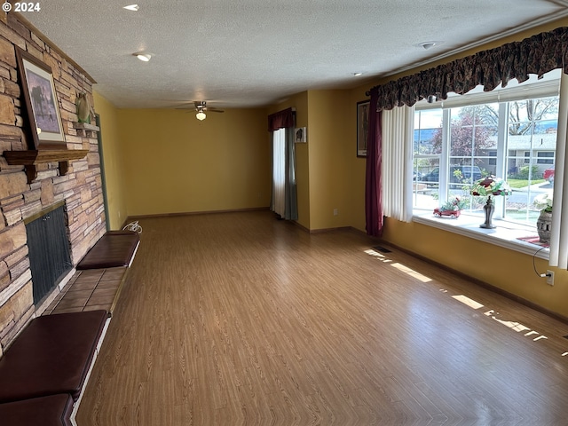 unfurnished living room featuring ceiling fan, a fireplace, hardwood / wood-style floors, and a textured ceiling