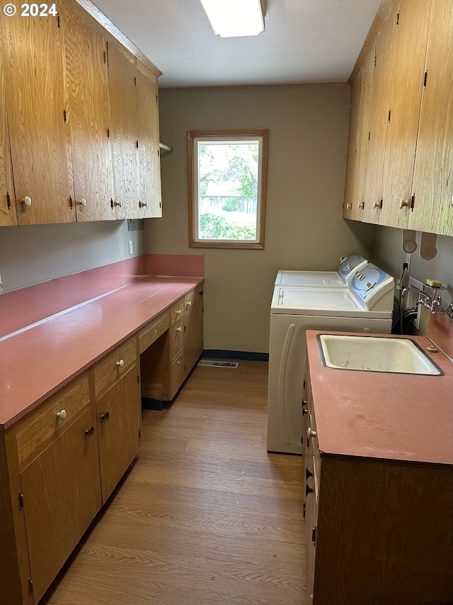 laundry room with cabinets, washing machine and clothes dryer, light hardwood / wood-style flooring, and sink