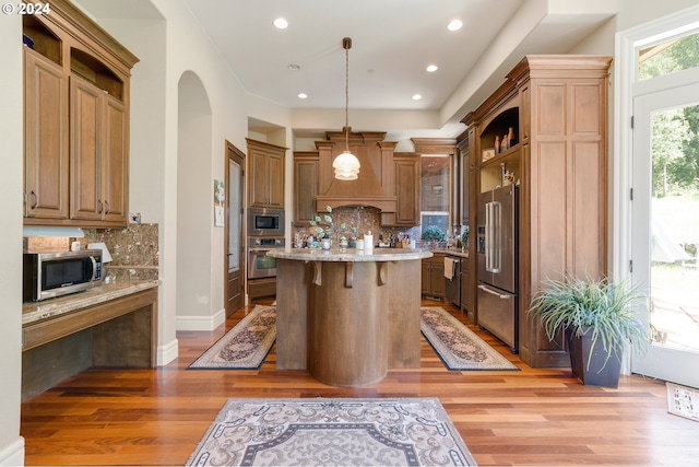 kitchen with a kitchen bar, backsplash, stainless steel appliances, a kitchen island, and hanging light fixtures